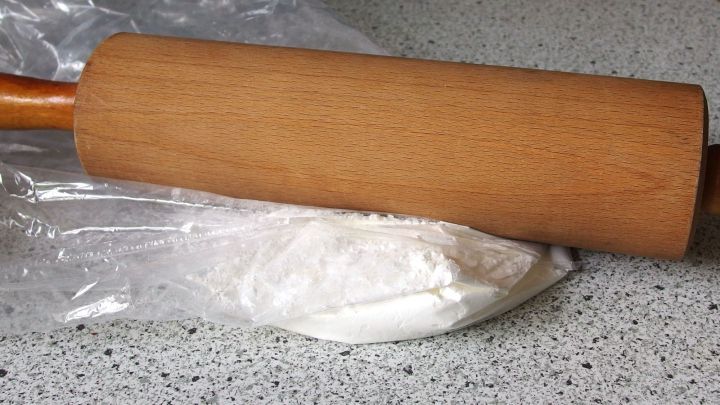 Ein Nudelholz liegt auf einem Haufen Puderzucker, bereit zum Ausrollen auf einer grauen Arbeitsfl&auml;che.