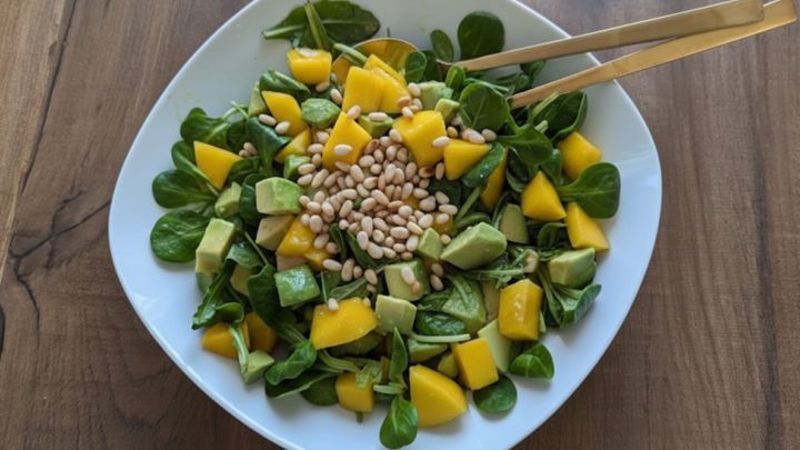 Avocado-Mango Salat mit Orangendressing: Auf dem Teller Feldsalat mit Avocado- und Mangow&uuml;rfeln, getoppt mit Pinienkernen.