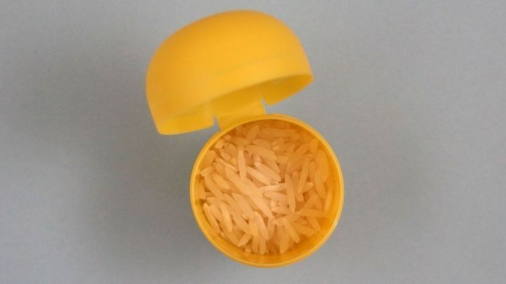 Eine gelbe &Uuml;-Ei-Plastikh&uuml;lle sitzt ge&ouml;ffnet und zeigt Reis im Inneren, der ein rasselndes Ger&auml;usch erzeugt.