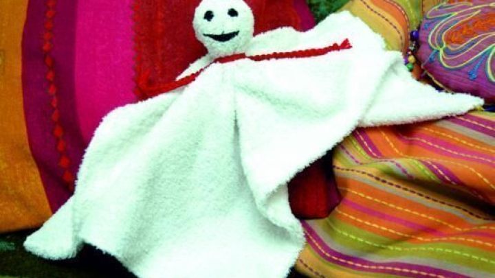 Ein selbstgemachtes kleines Nachtgespenst aus Stoff schwebt auf einem bunten Sofa aus gestreiften und gemusterten Decken.