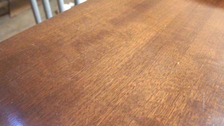 Ein Holzoberfl&auml;che zeigt Wasserflecken, die die nat&uuml;rliche Maserung beeintr&auml;chtigen, im Hintergrund unscharfe St&uuml;hle.