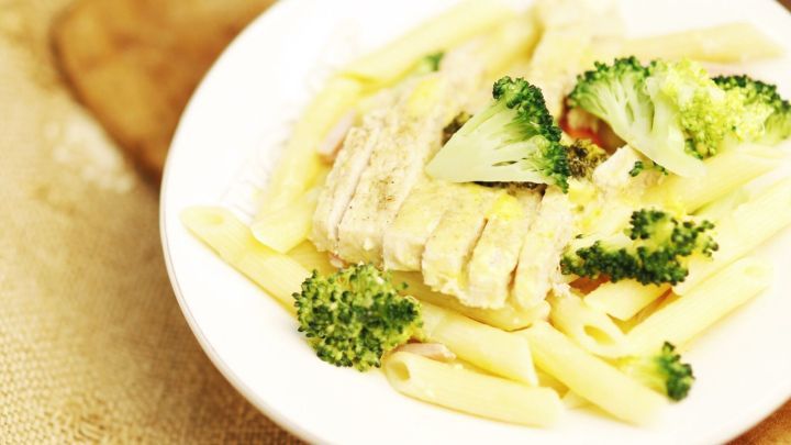 Ein Teller Nudeln mit H&auml;hnchen und Brokkoli in einer cremigen Curryso&szlig;e steht auf einem Holzbrett.