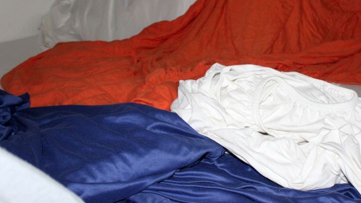 Bunte alte Bettlaken liegen &uuml;bereinander auf einem Bett, wobei die Farben rot, blau und wei&szlig; dominieren.