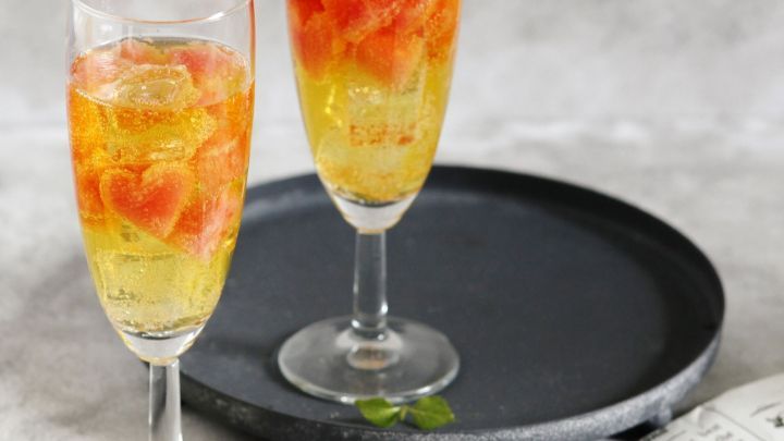 Zwei Gl&auml;ser mit Melonensekt stehen auf einem schwarzen Teller, umgeben von einer Zeitung und einer Brille.