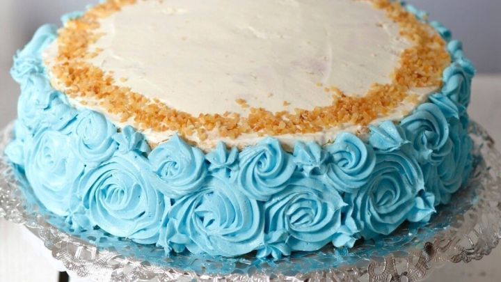 Eine Torte mit blauer Buttercreme und dekorativen rosafarbenen R&ouml;schen steht auf einem Kuchenteller, bereit zum Servieren.