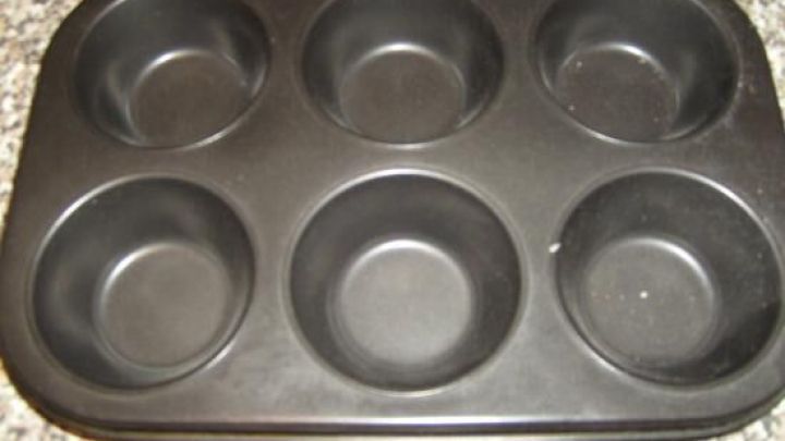 Eine schwarze Muffinform, die auf einer gemusterten Arbeitsplatte steht, bietet Platz f&uuml;r sechs gef&uuml;llte Paprikaschoten.