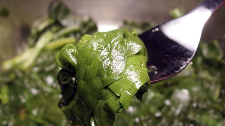 Ein St&uuml;ck frischer Spinat wird mit einer Gabel angehoben und zeigt die saftige gr&uuml;ne Farbe, die oft mit hohem Eisengehalt assoziiert wird.