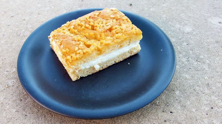 Ein St&uuml;ck Bienenstich liegt auf einem schwarzen Teller und zeigt die luftige, goldene Oberseite des Kuchens.