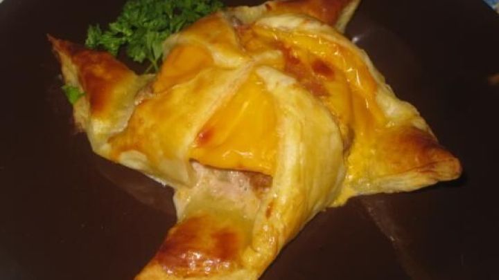 Bl&auml;tterteig mit Hackfleisch und K&auml;se gef&uuml;llt, liegt auf einem dunklen Teller mit Petersilie garniert.