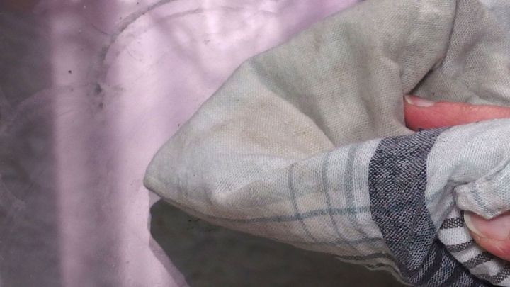 Ein Handtuch wischt &uuml;ber ein gl&auml;nzendes Fenster, um es streifenfrei zu reinigen, w&auml;hrend Licht reflektiert wird.