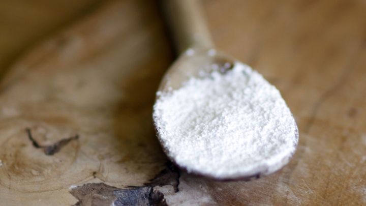 Ein Holzl&ouml;ffel h&auml;lt ein wenig Kaiser Natron, w&auml;hrend er auf einer rustikalen Holzoberfl&auml;che liegt.