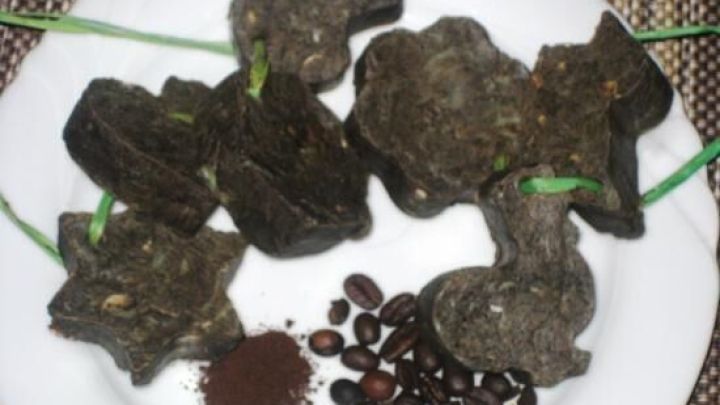 Kaffee-Seife in verschiedenen Formen liegt auf einem Teller neben Kaffeebohnen und gemahlenem Kaffee auf einer Tischdecke.