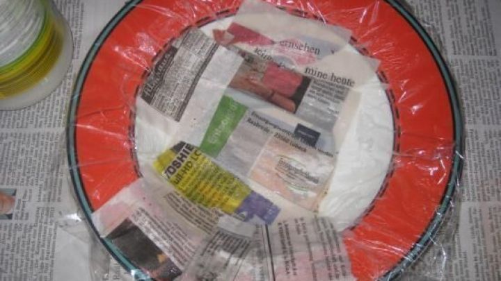 Ein runder Deko-Teller aus Pappmachee wird mit Zeitungspapier ausgelegt und in einer Werktisch-Umgebung vorbereitet.