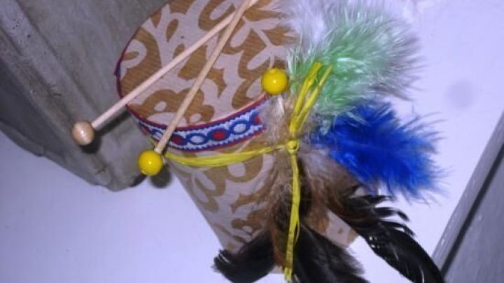 Eine kreativ dekorierte Indianertrommel aus einer Konservendose steht auf einem Tisch, geschm&uuml;ckt mit Federn und Perlen.