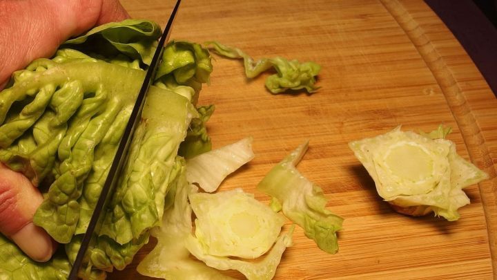 Ein gr&uuml;nes Salatherz wird mit einem Messer auf einem Holzbrett geschnitten, w&auml;hrend einige Bl&auml;tter abfallen.