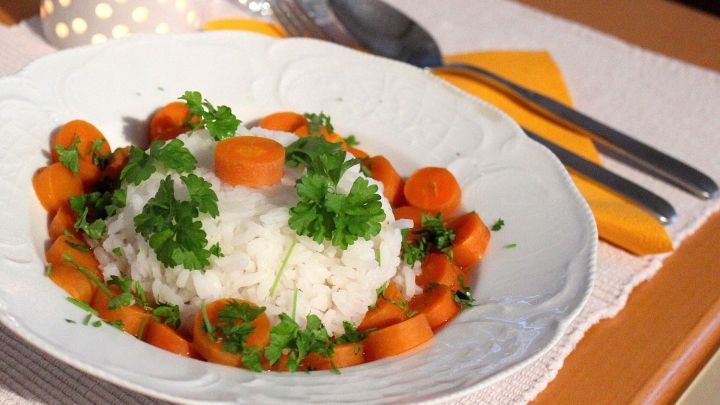 Ein Teller Reis mit Koriander und M&ouml;hren befindet sich auf einem Tisch, umgeben von Besteck und einem dekorativen Tuch.