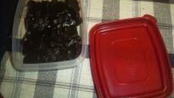 Schwarze, zuckerfreie Lakritzst&uuml;cke liegen in einer transparenten Box neben dem roten Deckel auf einem karierten Tuch.