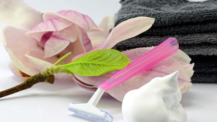 Ein Rasierer liegt auf einem Handtuch, umgeben von einer Bl&uuml;te und einer Schaummasse, ideal f&uuml;r eine pickelfreie Bikinizone.