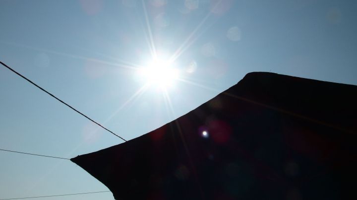 Ein Sonnenschein strahlt &uuml;ber einem Sonnenschirm, der Schatten auf den Boden wirft, w&auml;hrend der Himmel klar ist.