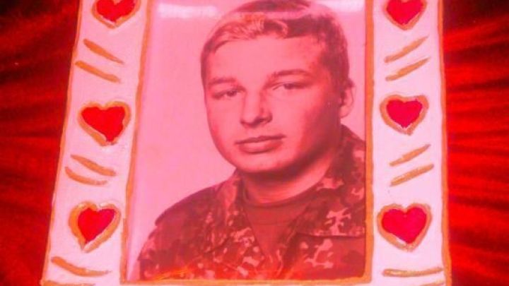 Ein Bilderrahmen aus Styropor, geschm&uuml;ckt mit roten Herzen, h&auml;lt ein Portr&auml;t eines jungen Mannes im Milit&auml;runiform.