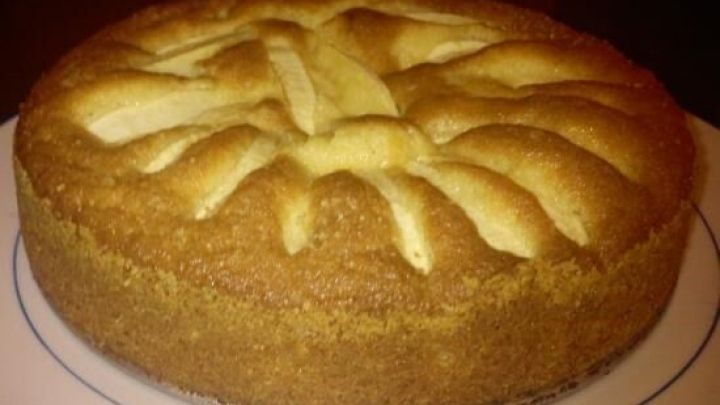 Ein goldbrauner Apfelschlupfkuchen ruht auf einem wei&szlig;en Teller, umgeben von heller Beleuchtung, mit gerasterten Apfelscheiben.