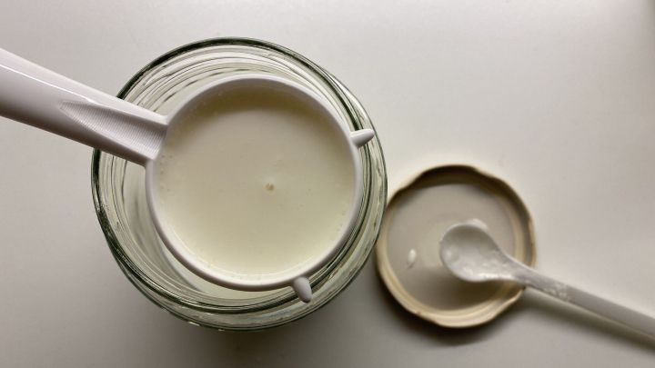 Ein Glas mit selbstgemachtem Kefir wird mit einem L&ouml;ffel abgehoben, um die cremige Konsistenz zu zeigen.