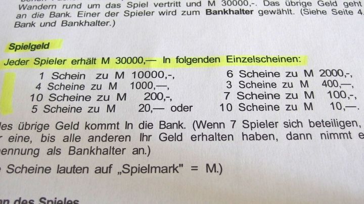 Ein Dokument zeigt Spielanleitungen, die mit einem Textmarker bearbeitet sind, und beschreibt den Geldverteilungsprozess.