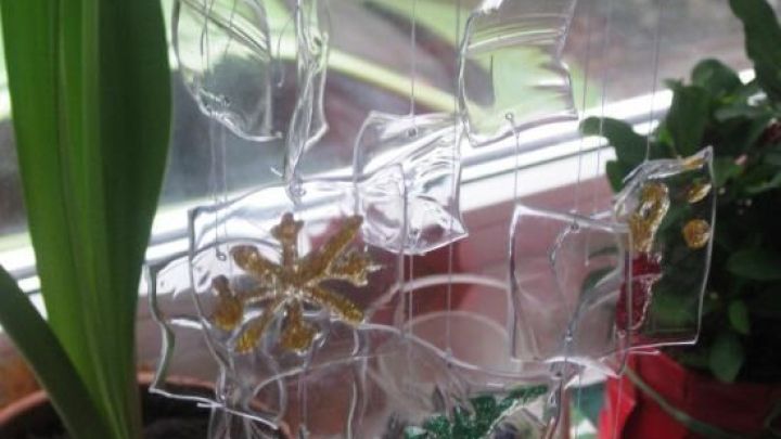 Ein Windspiel aus Kunststoffflaschen schwingt sanft im Raum, h&auml;ngen an einer Fensterbank, umgeben von gr&uuml;nen Pflanzen.