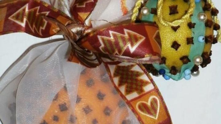 Duftkugeln aus Zitrusfr&uuml;chten h&auml;ngen dekorativ in einem Netz, gespickt mit Nelken, verziert mit festlichen B&auml;ndern.