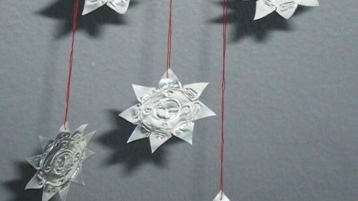 Sterne aus leeren Teelichth&uuml;llen h&auml;ngen an Schn&uuml;ren vor einer grauen Wand und schaffen eine festliche Atmosph&auml;re.