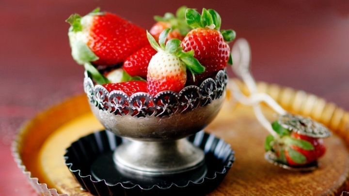 Frische Erdbeeren liegen in einer dekorativen Schale auf einem rustikalen Holzbrett, ideal f&uuml;r eine Erdbeer-Bowle.