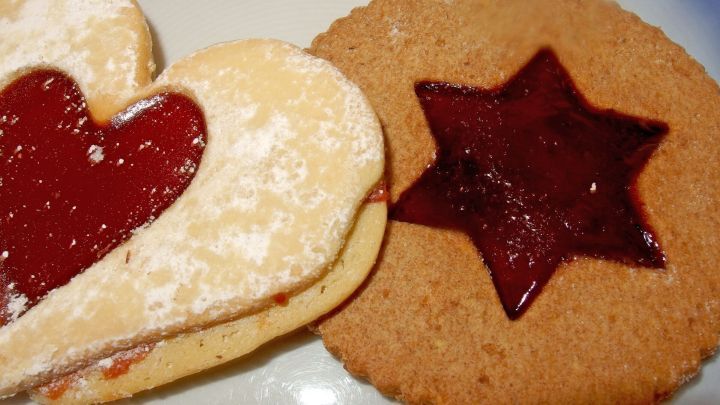 Zwei liebevoll dekorierte Pl&auml;tzchen liegen auf einem Teller, eines mit Herzform und das andere sternf&ouml;rmig, gef&uuml;llt mit Marmelade.