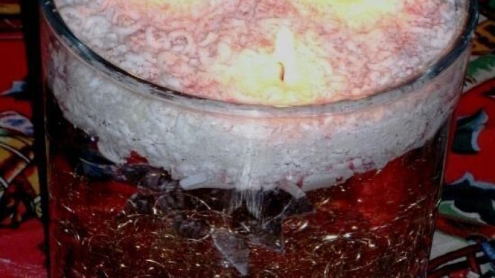 Kerzen brennen in einem Glasgef&auml;&szlig;, gef&uuml;llt mit Wachsgranulat, auf einem festlichen Tischtuch.