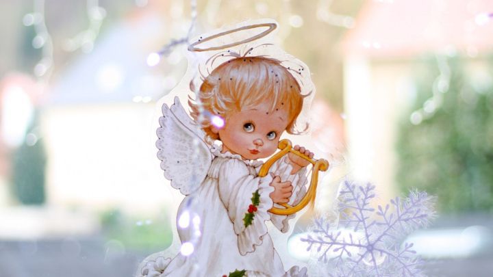 Ein Engel mit Trompete steht im Vordergrund, zart beleuchtet durch Fensterlicht, umgeben von glitzernden Schneeflocken.