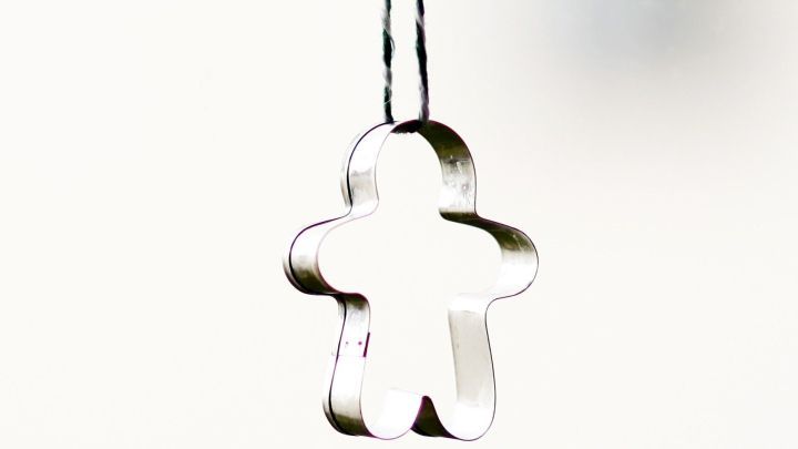 Ein Ausstechf&ouml;rmchen in Form eines Lebkuchenmanns h&auml;ngt an einem Faden vor einem weihnachtlich geschm&uuml;ckten Fenster.