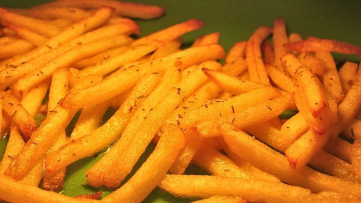 Knusprige Backofenpommes liegen auf einem gr&uuml;nen Teller und warten darauf, serviert zu werden.