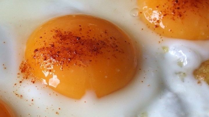 Saftige Spiegeleier mit leuchtend gelben Eigelben, bestreut mit Paprika, liegen auf einem wei&szlig;en Teller.