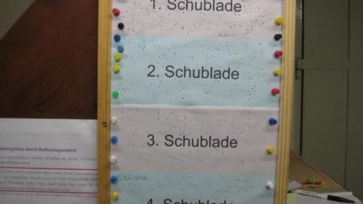 Ein Schild mit Listen zum Einr&auml;umen eines Gefrierschranks, unterteilt in "1. Schublade" bis "4. Schublade", h&auml;ngt an der Wand.