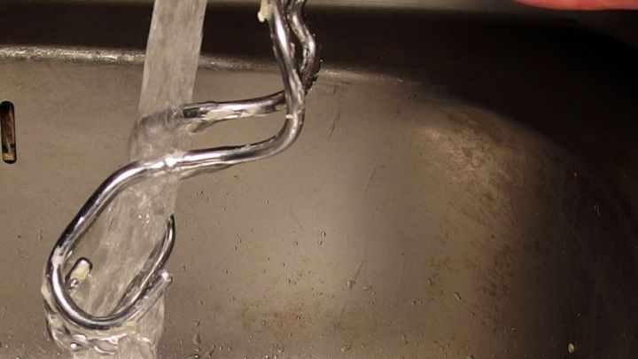 Ein silbernes K&uuml;chenwerkzeug wird unter kaltem Wasser in einem Sp&uuml;lbecken abgewaschen, um Teigreste zu entfernen.