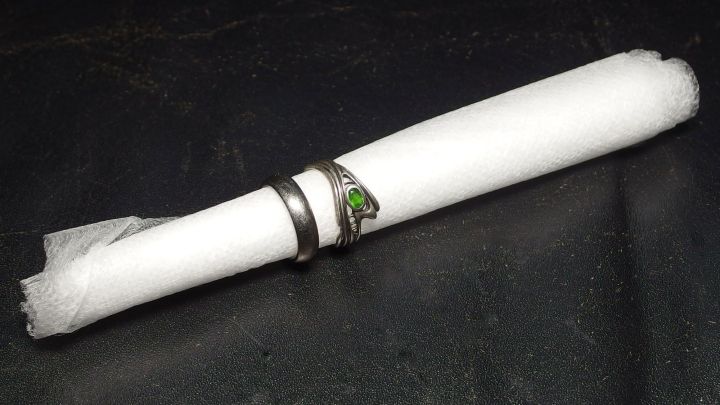 Auf einem schwarzen Untergrund liegen mehrere Ringe um eine zusammengerollte, wei&szlig;e Serviette, die sanft aufbewahrt wird.