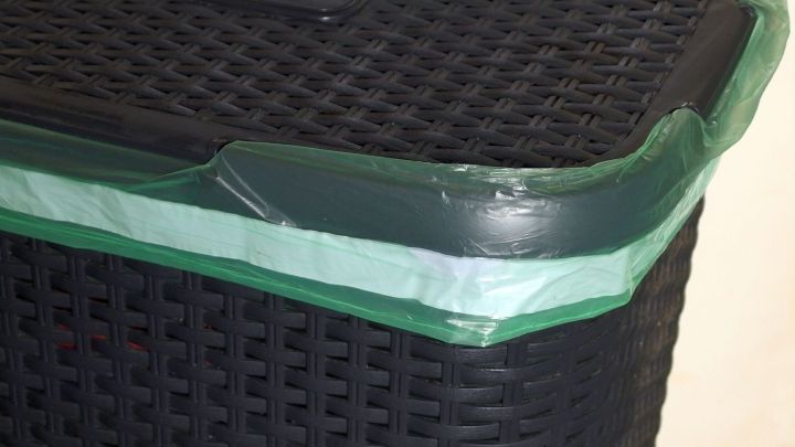 Ein schwarzer, geflochtener M&uuml;lleimer mit einem gr&uuml;nen Rand, der bereit ist, M&uuml;ll zu sammeln, steht auf einem hellen Boden.