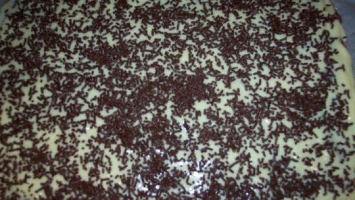 Eine gl&auml;nzende Schokoglasur bedeckt einen kuchenartigen Untergrund, der mit Schokoladenstreuseln dekoriert ist.