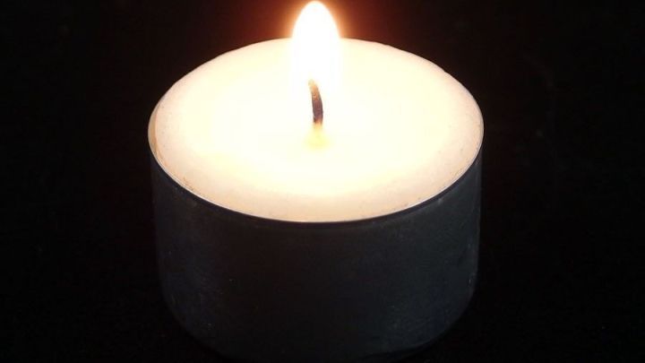 Eine brennende Kerze mit Docht leuchtet sanft auf einem schwarzen Untergrund und erzeugt eine beruhigende Atmosph&auml;re.