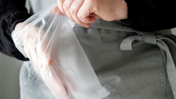 Eine Hand zieht sich einen durchsichtigen Einweghandschuh &uuml;ber, w&auml;hrend sie eine Sch&uuml;rze tr&auml;gt, um beim Kuchenbacken sauber zu bleiben.