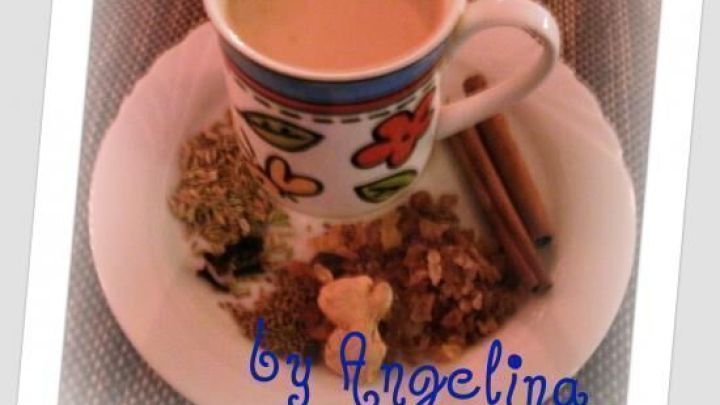 Tasse Chai auf einem Teller, umgeben von Gew&uuml;rzen wie Zimt. Text: "by Angelina".