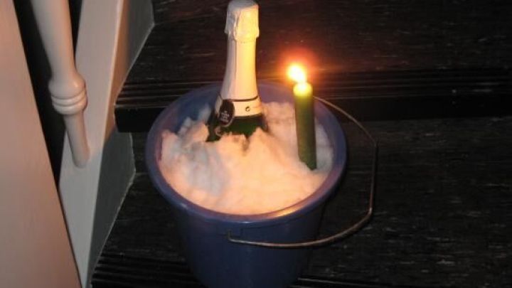 Sektflasche k&uuml;hlt im Schnee-Eimer auf einer Treppenstufe, daneben brennt eine Kerze, die f&uuml;r stimmungsvolles Licht sorgt.