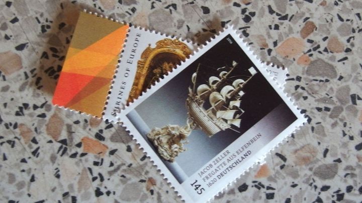 Zwei zusammenklebende Briefmarken liegen auf einem bunten, strukturierten Untergrund und warten darauf, getrennt zu werden.