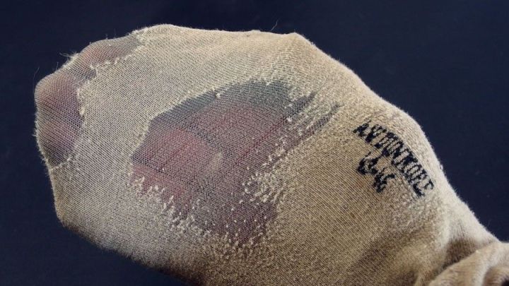 Wollstr&uuml;mpfe zeigen eine durchgescheuerte Stelle, w&auml;hrend sie auf einem dunklen Hintergrund liegen, was ihre Langlebigkeit hervorhebt.