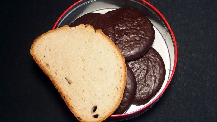 Ein St&uuml;ck Brot liegt neben einer Auswahl an Pl&auml;tzchen in einer roten Dose auf schwarzem Hintergrund.