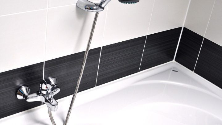 Eine gl&auml;nzende Duscharmatur steht &uuml;ber einer wei&szlig;en Badewanne, umgeben von grauen und wei&szlig;en Fliesen, m&ouml;glicherweise mit Kalk.